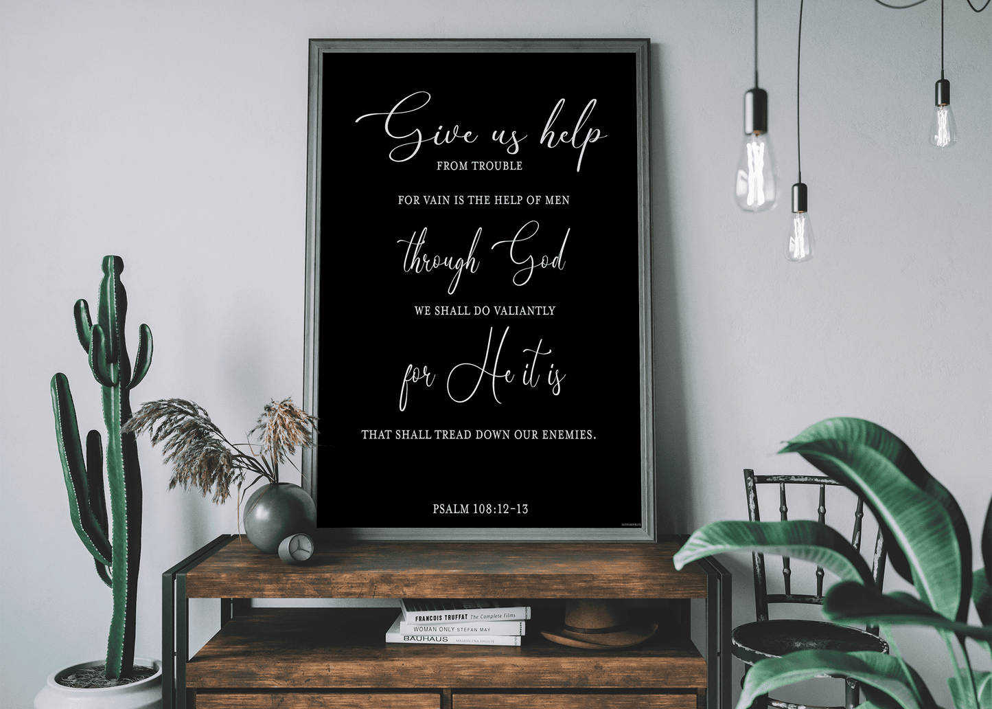 A wooden console table adorned with plants and a black framed art print of Psalm 108:12-13 by Olive Grove Life.