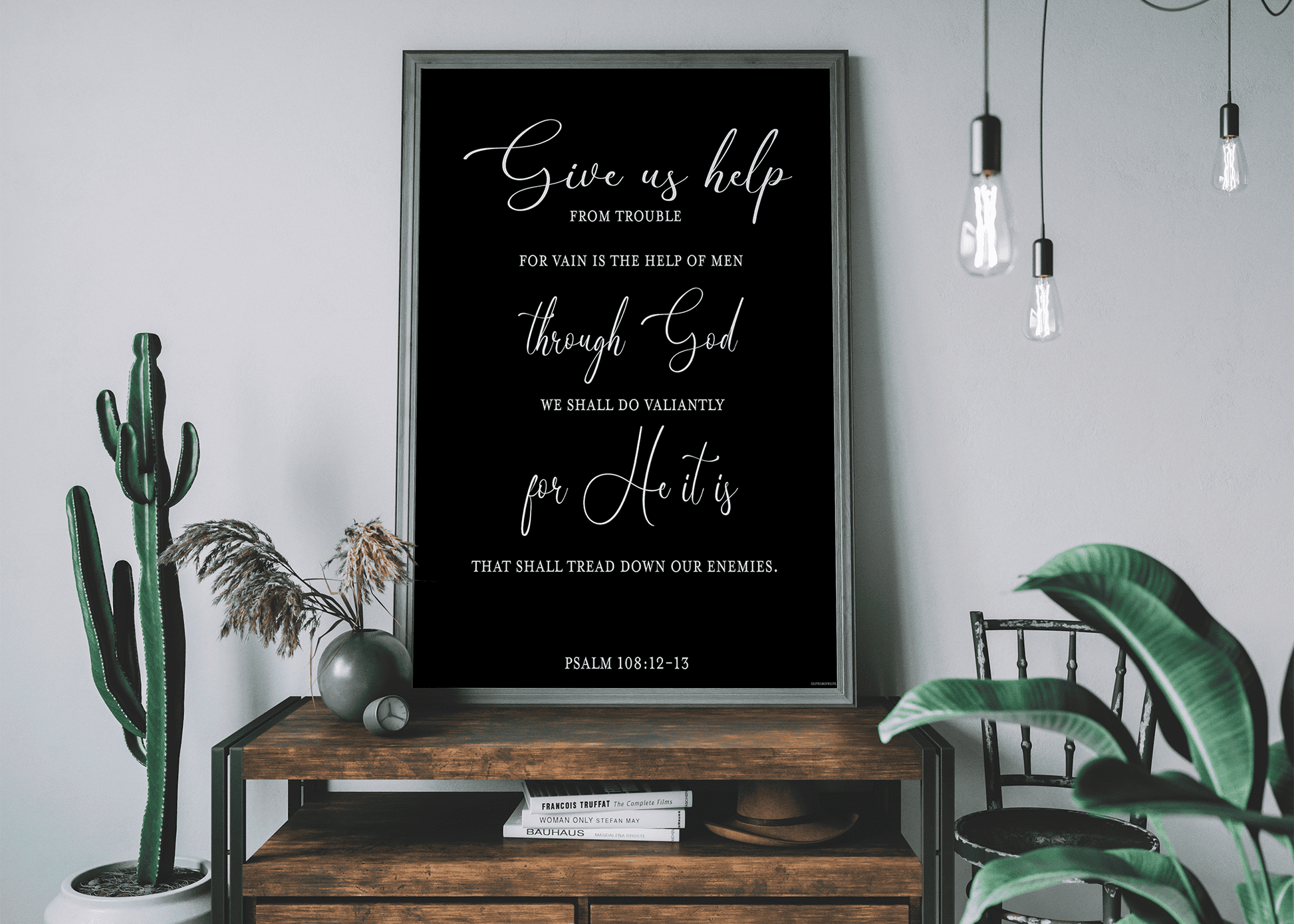 A wooden console table adorned with plants and a black framed art print of Psalm 108:12-13 by Olive Grove Life.