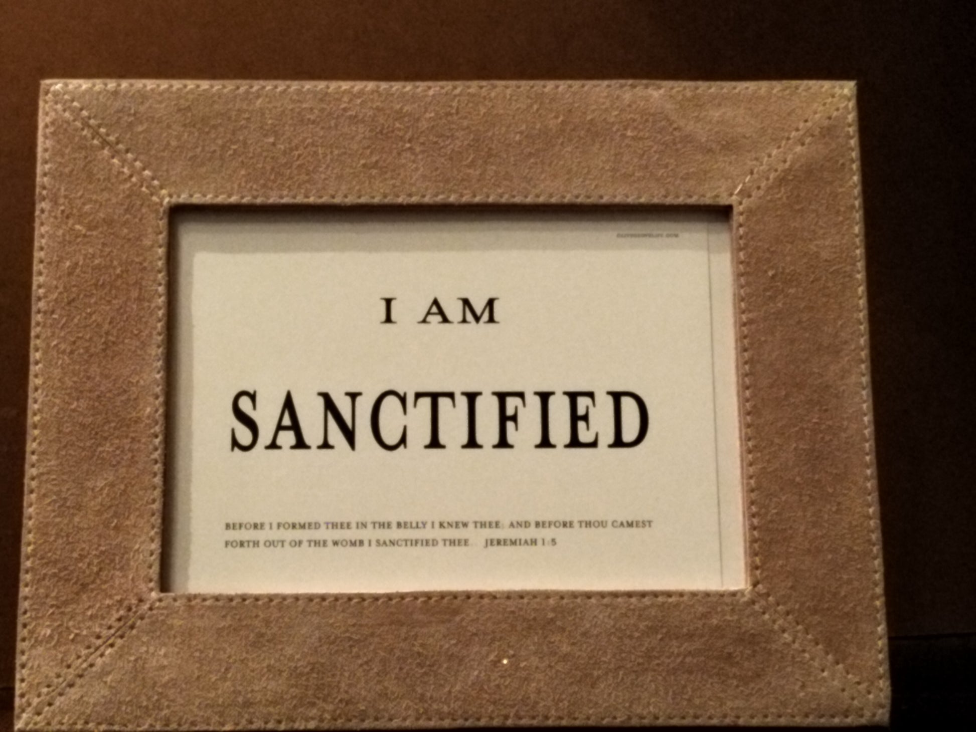 Framed text 'I AM SANCTIFIED' in a brown frame on a dark background